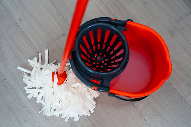 red wet cleaning bucket with water wringer and mop on floor with grey floor covering
